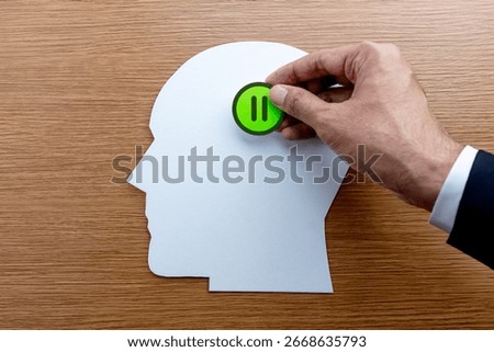 A head-shaped cutout and a green button with a pause symbol. Pausing, taking a break, stress management, and mindfulness concept. 