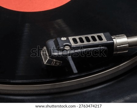 A headshell with an electromagnetic head of a vinyl record player mounted on it against the background of a gramophone record.