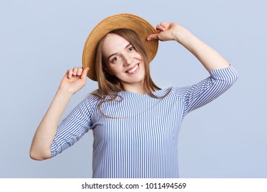 Headshot of adorable pretty young woman wears straw hat and striped blouse, being in good mood, rejoices coming vacations, going to spend them in tropical country abroad together with boyfriend