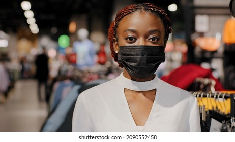 Headshot African American Alone Serious Girl Woman Shopper Consumer Female Consultant Salesperson In Medical Face Mask Looking At Camera Stands Indoors In Clothing Store Shopping Mall Covid Time