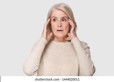 Headshot of aged woman feeling scared isolated on gray background. Portrait of old lady facing strong fear, being terrified to death. Elderly female having frightened grimace on face. People emotions