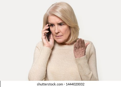 Headshot Of Annoyed Old Woman Having Argument Talking Via Smartphone. Angry Aged Female Speak Irritated By Cell Phone, Find Out Bad News Over Telephone. Portrait Of Lady With Mobile Isolated On Grey