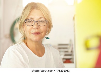 Headshot Of Attractive Senior Female With Fair Hair Dressed In Casual Clothes Standing Against Blurred Interior Background Of Her Apartment Getting Ready To Go Out For Morning Walk With Her Friend