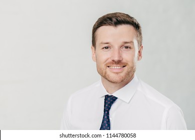 Headshot Of Attractive Unshaven Young Male With Cheerful Expression, Looks Confidently At Camera, Being Pleased To Meet With Colleagues, Dressed In Formal Clothes, Isolated Over White Background