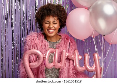 Headshot of beautiful pleased dark skinned model with gentle makeup, laughs sincerely, holds balloons, spends free time on shindig , dressed in fashionable outfit. Party decorations concept. - Shutterstock ID 1361561519