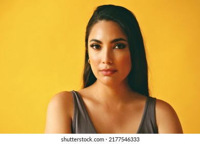 Headshot Beauty Shot Of Hispanic Latina Woman Thoughtful Young Adult With Black Long Hair And Tank Top In Front Of Yellow Background Looking At Camera Studio Shot