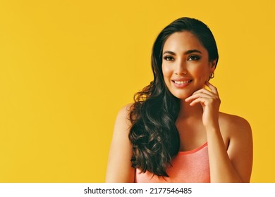 Headshot Beauty Shot Of Thoughtful Sensual Smiling Hispanic Latina Woman Young Adult With Hand On Chin Black Long Hair And Tank Top In Front Of Yellow Background Looking Away At Copy Space Studio Shot