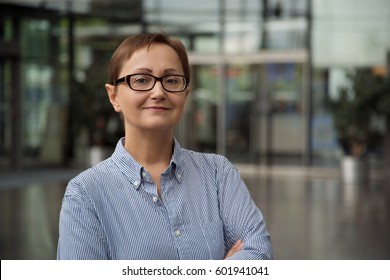 Headshot Of Business Woman In The Office Background Portrait Of Older Women Wearing Glasses And Oxford Long Sleeve Striped Shirt. Caucasian Brunette Female With Short Haircut In Her 40s 50s Years Old 