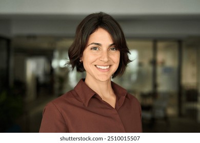 Headshot close up face portrait of young happy smiling Hispanic businesswoman, female company worker or corporate manager, confident business woman entrepreneur looking at camera at work in office.