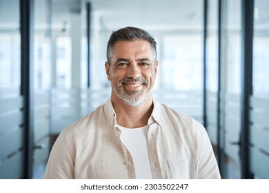 Headshot close up portrait of indian or latin confident mature good looking middle age leader, ceo male businessman on blur office background. Handsome hispanic senior business man smiling at camera.