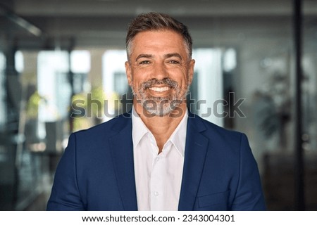 Headshot close up portrait of indian or latin confident mature good looking middle age leader, ceo male businessman in suit on office background. Handsome hispanic senior business man smile at camera.