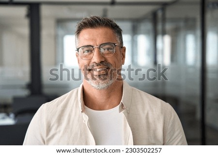 Headshot close up portrait of latin confident mature good looking indian middle age leader, ceo male businessman on blur office background. Handsome hispanic senior business man smiling at camera.