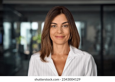 Headshot close up portrait of latin hispanic confident mature good looking middle age leader, ceo female businesswoman on blur office background. Gorgeous beautiful business woman smiling at camera.