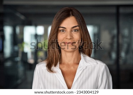 Headshot close up portrait of latin hispanic confident mature good looking middle age leader, ceo female businesswoman on blur office background. Gorgeous beautiful business woman smiling at camera.