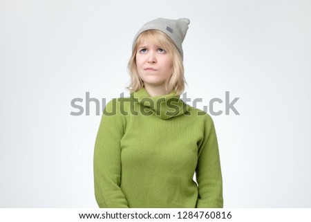 Headshot of doubtful and indecisive teenage girl in hat looking up with thoughtful pensive expression, thinking or dreaming of something