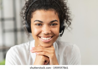 Headshot of friendly African American millennial woman in a headset sitting with her hands on a chin, working in the customer service department as call center operator, helping client with inquiry
