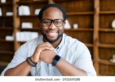 Headshot Of Friendly And Confident African-American Guy Wearing Stylish Eyeglasses And Smart Casual Wear, Looks At The Camera And Holds Hands In The Lock Near Chin. Employee Profile