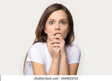 Headshot of frightened woman looking at fear eyes wide open. Studio portrait of terrified, stressed, scared to death young female biting her finger isolated on gray background. People emotions concept