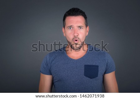 Headshot of goofy surprised bug-eyed young man student wearing casual blue  t-shirt staring at camera with shocked look, expressing astonishment and shock, screaming Omg or Wow