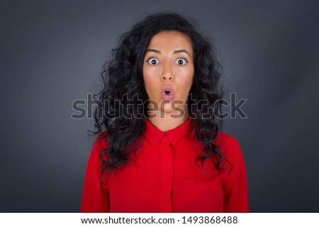Headshot of goofy surprised bug-eyed young woman student wearing casual red shirt staring at camera with shocked look, expressing astonishment and shock, screaming Omg or Wow