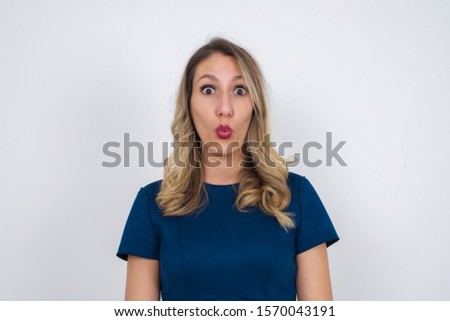 Headshot of goofy surprised bug-eyed young woman student wearing blue dress staring at camera with shocked look, expressing astonishment and shock, screaming Omg or Wow