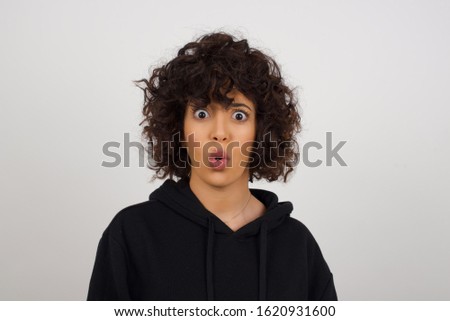 Headshot of goofy surprised  young woman student wearing black sweatshirt staring at camera with shocked look, expressing astonishment and shock, screaming Omg or Wow