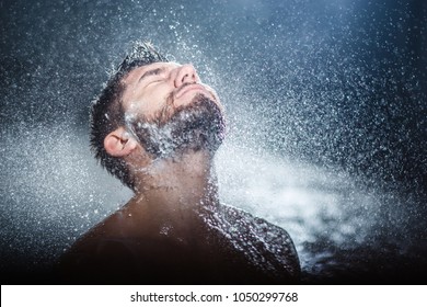 Headshot of a handsome fashionable young man taking shower, with water splashes all over