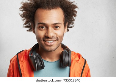 Headshot Of Handsome Mixed Race Male With Bushy Hair, Has Good Mood After Listening Loud Rock Music, Smiles Happily, Demonstrates White Perfect Teeth. People, Leisure And Entertainment Concept