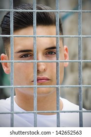 Headshot Of Handsome Young Man Caged Behind Metal Or Steel Grid