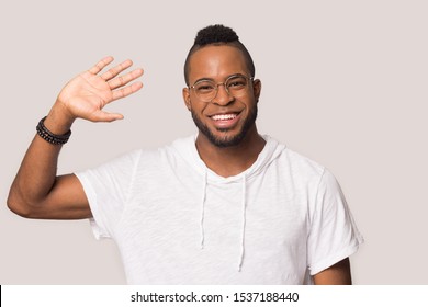 Headshot Of Happy African American Millennial Male Wear Glasses Isolated On Grey Studio Background Look At Camera Waving, Smiling Biracial Man Blogger Influencer Greeting Say Hello To Audience