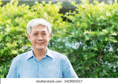 Headshot of happy old mature asian with white grey hair man wearing blue shirt smiling positive and looking at camera in garden outside the house. Senior asian male portrait with retirement concept.