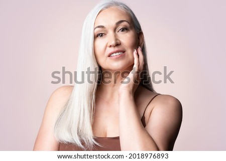 Headshot middle aged elderly gray-haired female looking at camera. Positive single mature senior retired woman touching healthy groomed perfect face skin. Natural old beauty and aging concept.