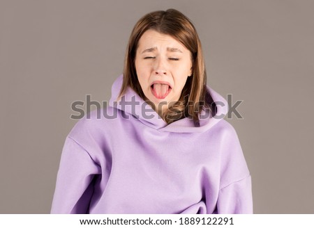 Headshot of naughty girl of European appearance sticking out tongue, trying to tease someone, looking immature and offensive, all her appearance expressing rudeness and disgust. Signs, symbols