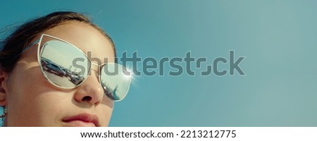 Headshot photography of attractive young woman wearing big sunglasses on blue sky background close up view