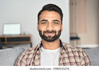 Headshot Portrait Of Attractive Confident Indian Hispanic Man Looking At Camera Sitting On Couch At Modern Living Room. Latin Businessman Posing In Casual Stylish Look At Home Office.