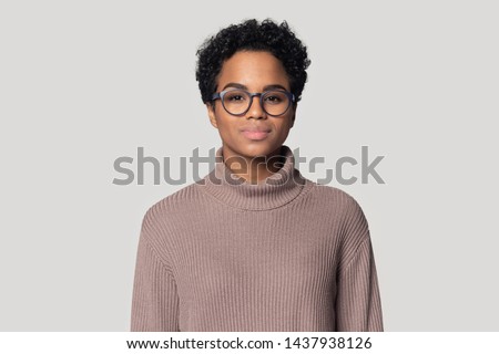 Headshot portrait of beautiful african American millennial woman in glasses and sweater stand isolated on grey studio background, black biracial female wearing spectacles look at camera posing