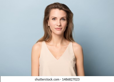 Headshot Portrait Of Beautiful Millennial Woman Isolated On Blue Studio Background Looking At Camera, Picture Of Pretty Attractive Young Female Model Posing Indoors Against Blank Wall