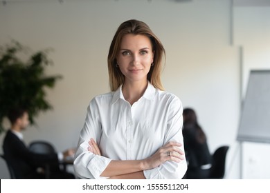 Headshot portrait of confident young businesswoman stand forefront with arms crossed looking at camera, successful millennial female ceo or boss posing for picture in office, leadership concept - Shutterstock ID 1555511204