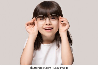 Headshot Portrait Of Cute Little Preschooler Girl Isolated On Grey Studio Background Wear Glasses Look At Camera, Small Child Try Spectacles At Opticians, Kid Eyesight Correction Treatment Concept