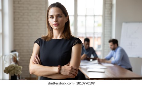 Headshot Portrait Of Focused Caucasian Young Businesswoman Stand Forefront Posing At Company Office Meeting, Serious Millennial Female Boss Or CEO Look At Camera Show Confidence And Success