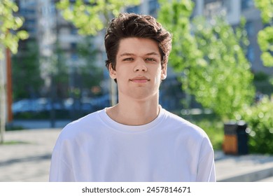 Headshot portrait of handsome guy 19, 20 years old, looking at camera outdoors - Powered by Shutterstock