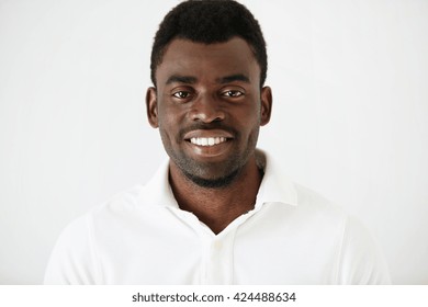 Headshot portrait of handsome young African American man  with a beard wearing white blank T-shirt looking and smiling  at the camera against white studio wall background. People and lifestyle concept