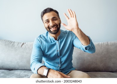 Headshot Portrait Of Handsome Young Indian Business Man With Friendly Confident Smile Feeling Happy And Positive Waving To Camera Saying Hello With Raised Hand Gesture Making Video Call. Webcam View