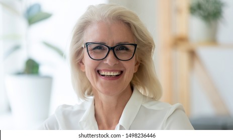 Headshot portrait of happy aged grey-haired businesswoman in glasses look at camera with toothy wide smile, close up of overjoyed senior woman boss or ceo in spectacles posing for picture