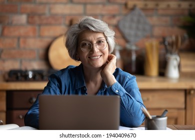 Headshot portrait of happy senior aged hispanic female sit at desk use laptop work study distantly. Confident old age woman remote worker freelancer look at camera at home office workplace at kitchen - Powered by Shutterstock