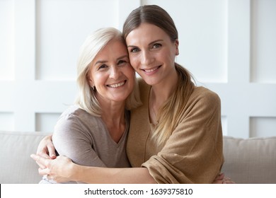 Headshot Portrait Of Happy Senior Mom And Adult Daughter Hug Sitting On Sofa At Home Look At Camera Smiling, Family Picture Of Mature Mother And Grownup Woman Child Posing For Photo Together