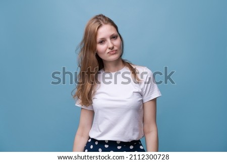 Headshot portrait happy young woman in white t-shirt and polka dot skirt smiling posing while looking at camera. Blue background. Caucasian girl enjoying life
