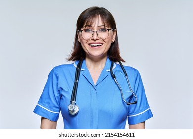 Headshot Portrait Of Nurse In Blue Uniform Looking At Camera On Light Studio Background