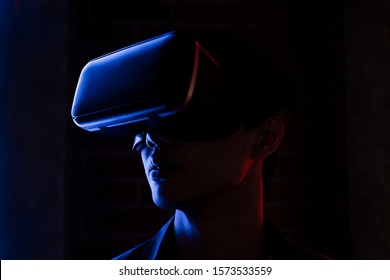 Headshot Portrait Of Smart Asian Gamer On VR Headset Under Blue And Red Neon Light In The Dark Room.