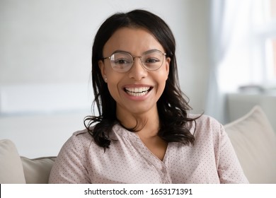 Headshot portrait of smiling African American young woman in glasses sit pose on couch in living room, profile picture of happy biracial confident female in spectacles relax on sofa at home laughing